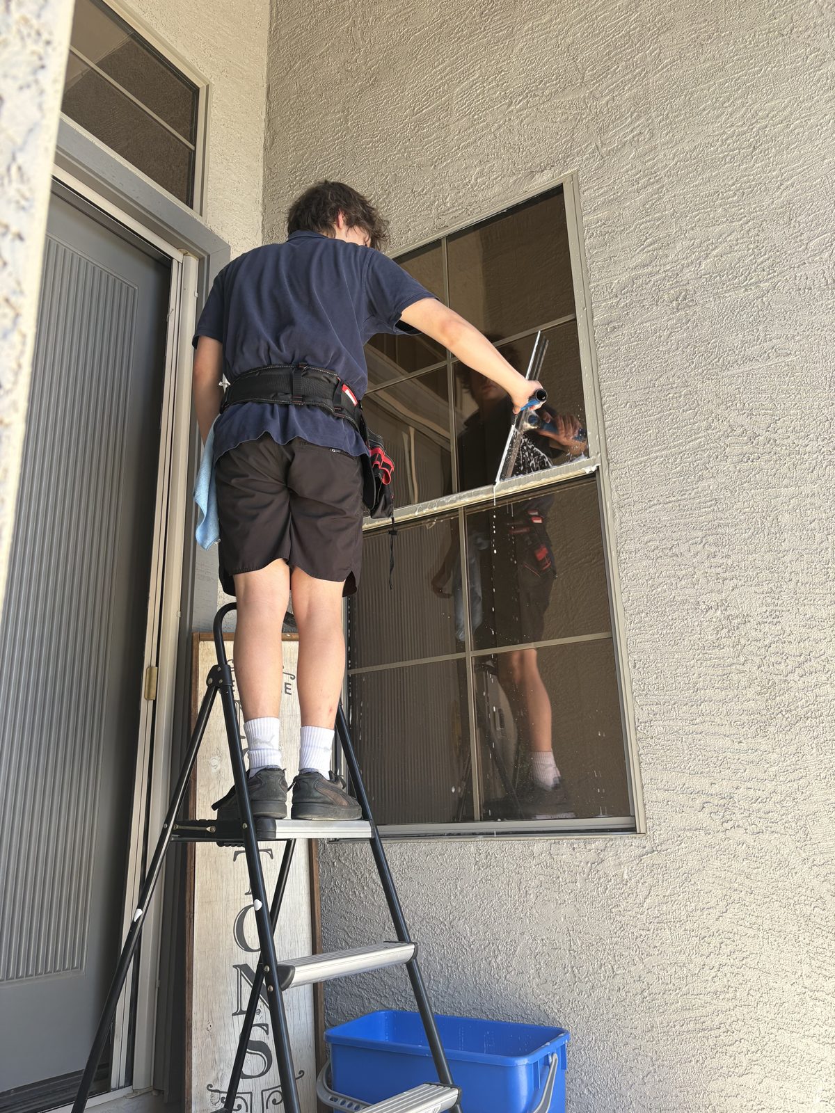 Cactus Clear Windows crew member squeegeeing a large exterior window from a ladder